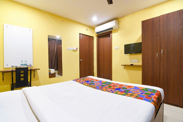 A hotel room with a bed, a desk, a chair, a wardrobe, and an air conditioning unit.