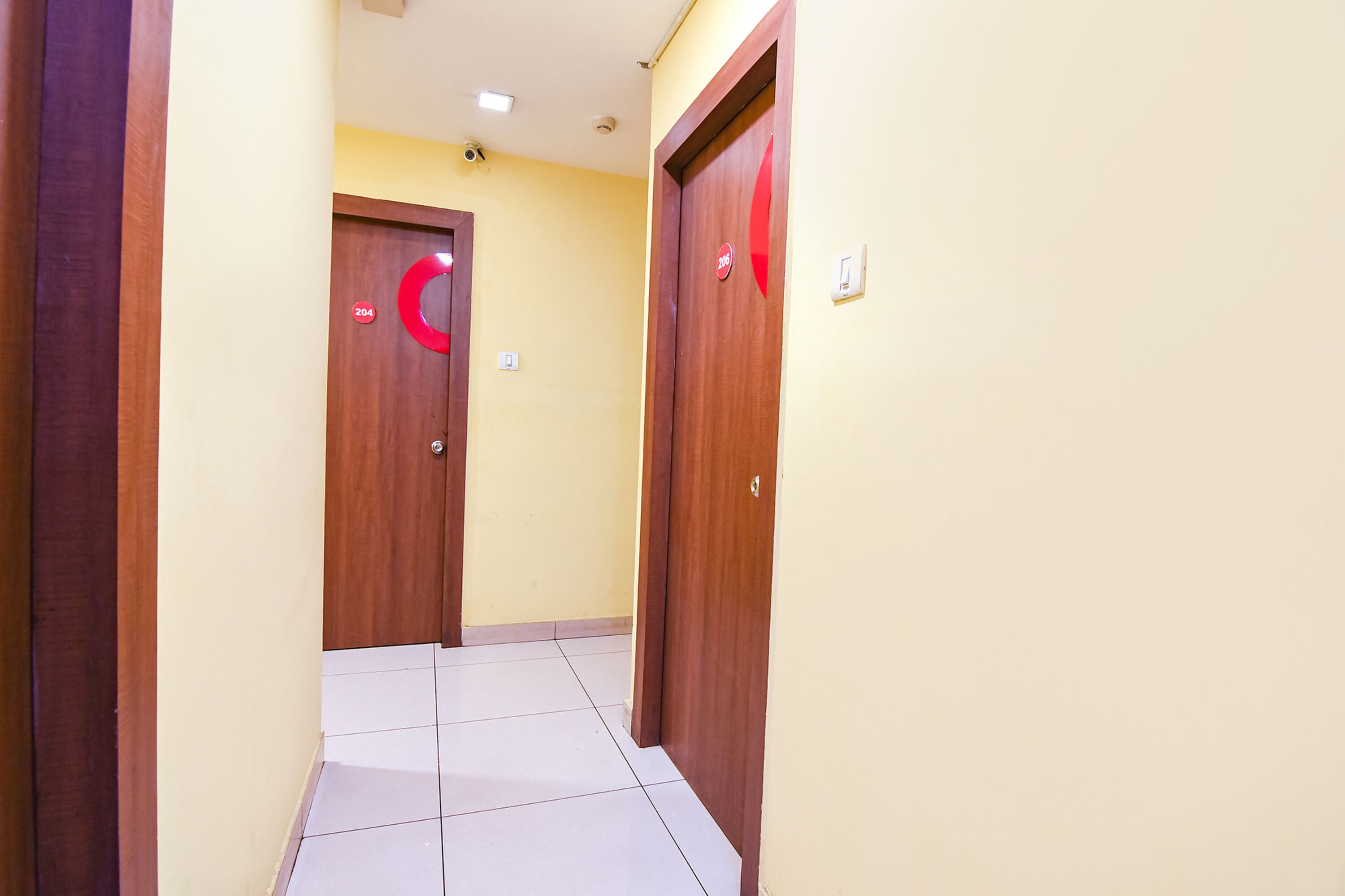 A hallway with two wooden doors, each marked with a red circular sign, and a tiled floor.