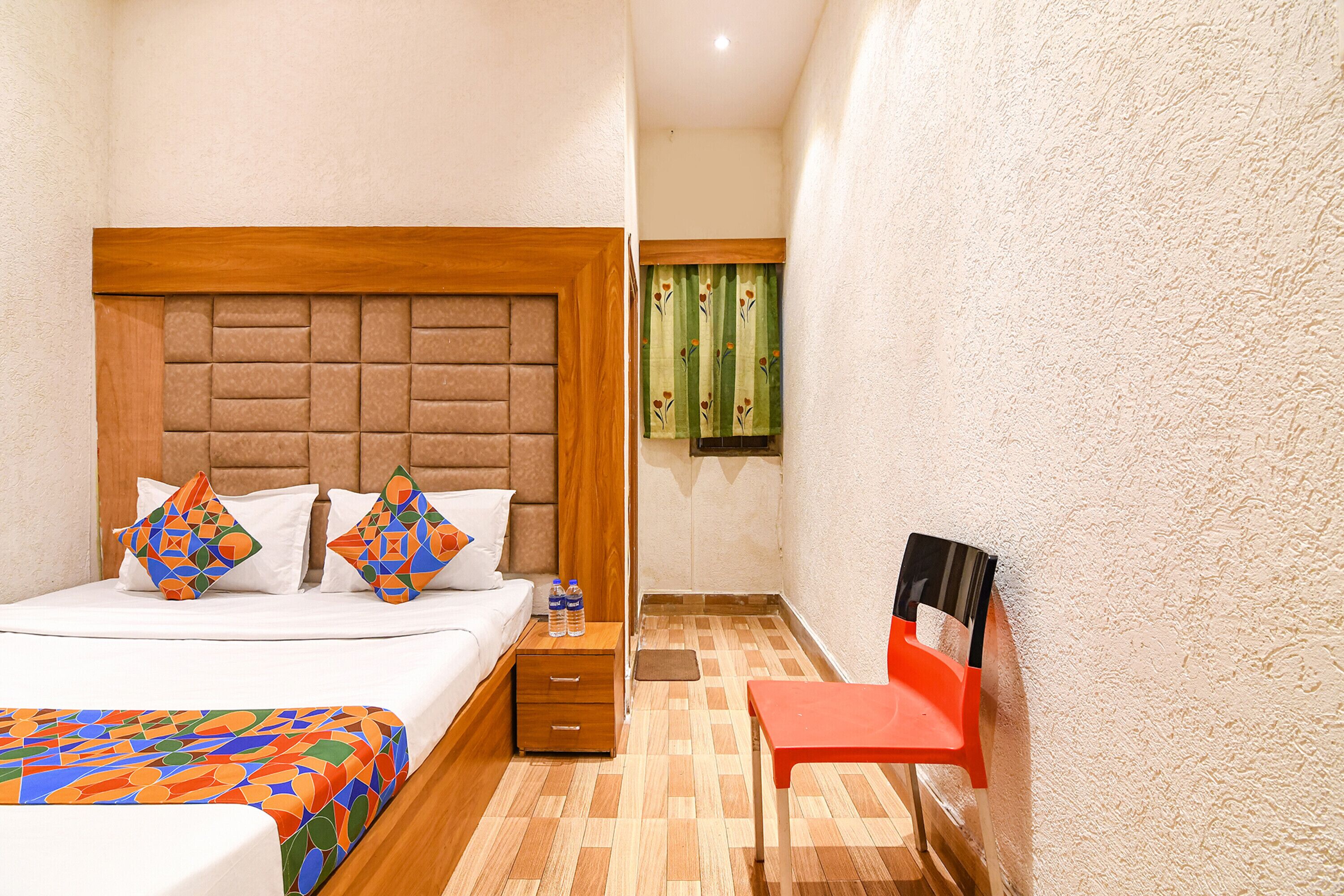 A hotel room with a bed, a nightstand, a chair, and a window with curtains.