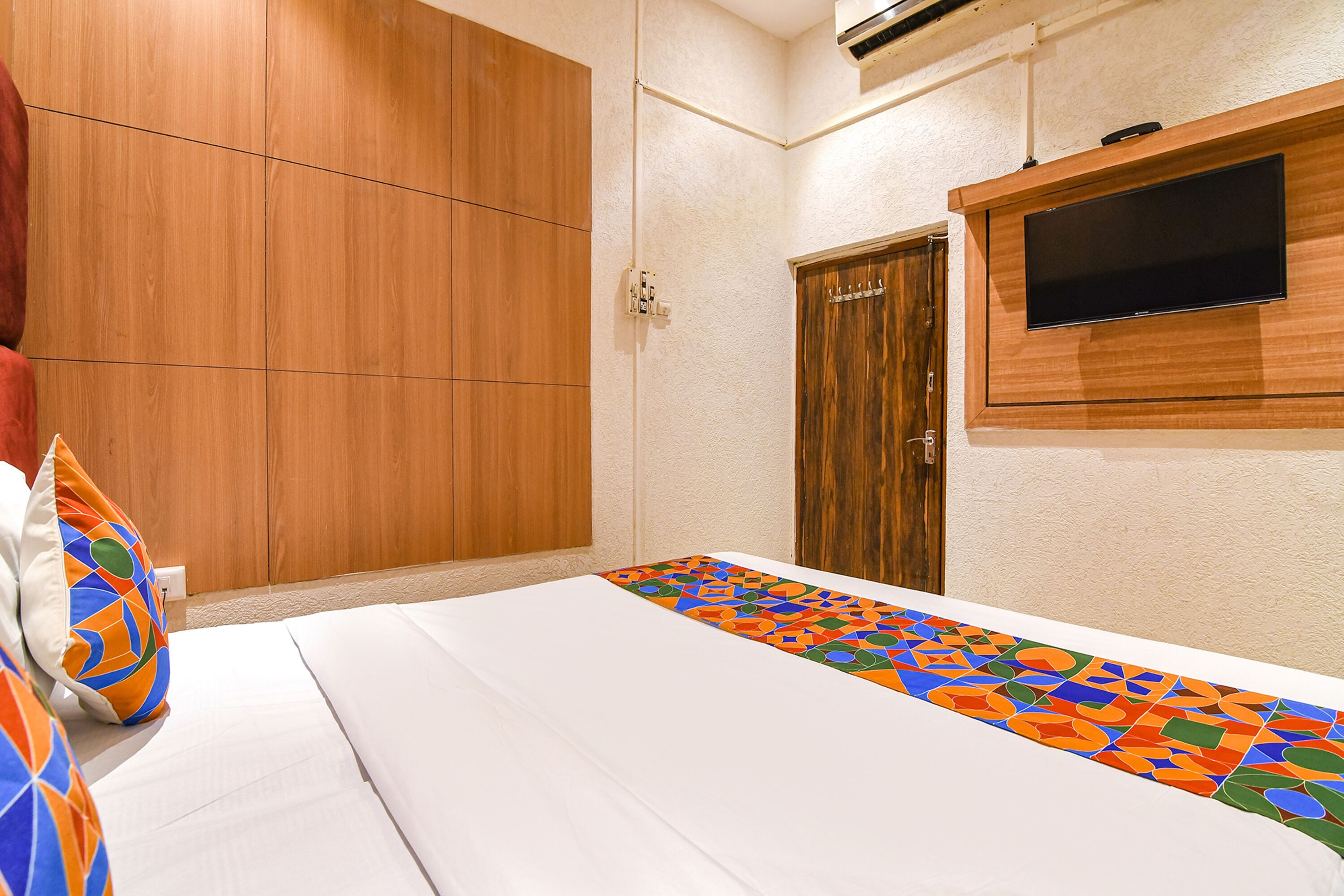 A hotel room with a large wardrobe, a flat-screen TV mounted on the wall, and a colorful runner on the bed.