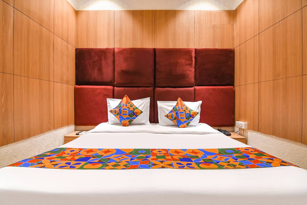 A hotel room with a large bed, a red upholstered headboard, and a colorful geometric-patterned bedspread.