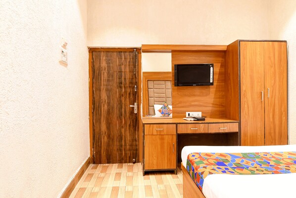A hotel room with a wooden wardrobe, a desk with a television, and a bed with a colorful bedspread. - FabHotel Marina (Kolkata)