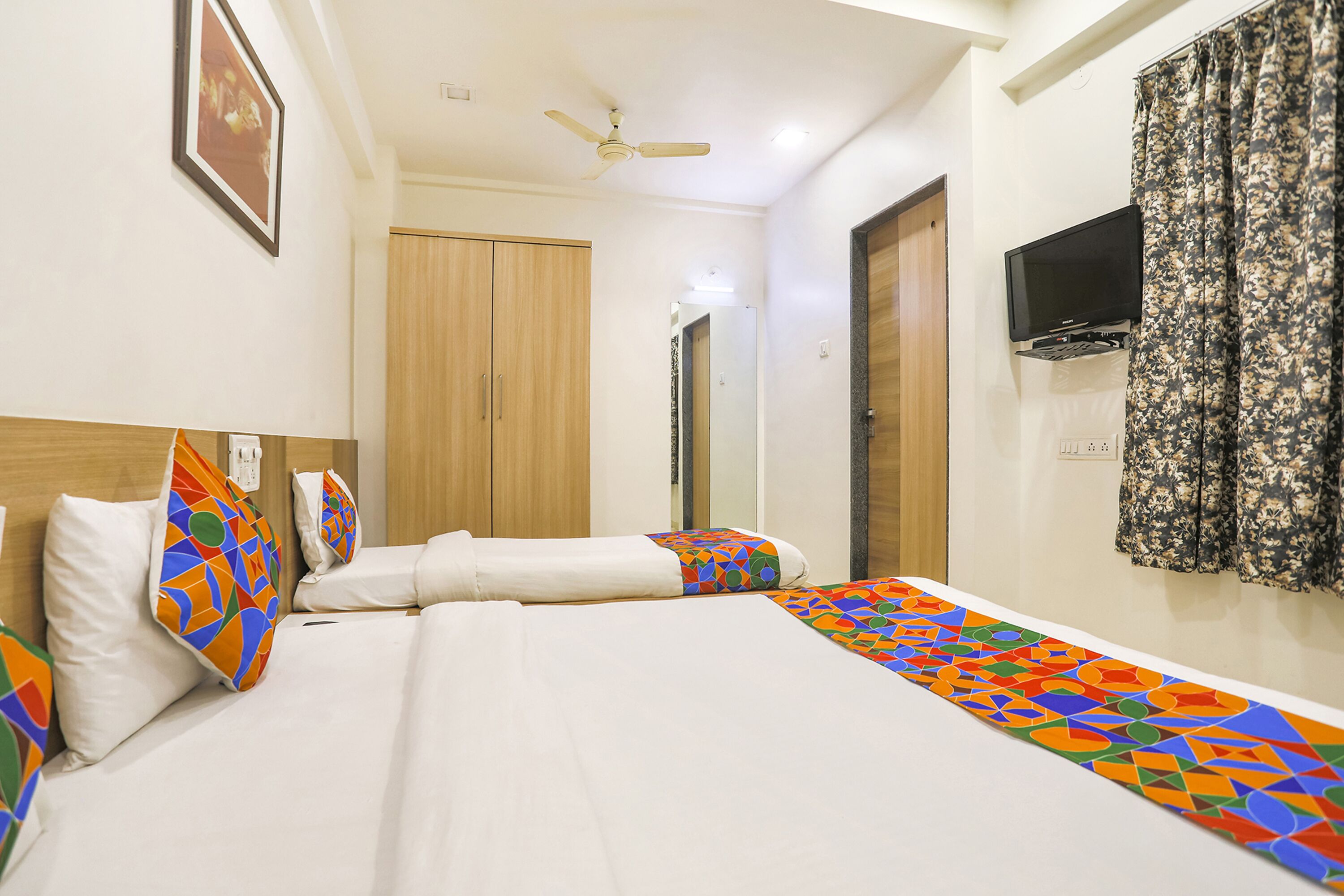 A hotel room with a bed, pillows, a ceiling fan, a television, and a door.
