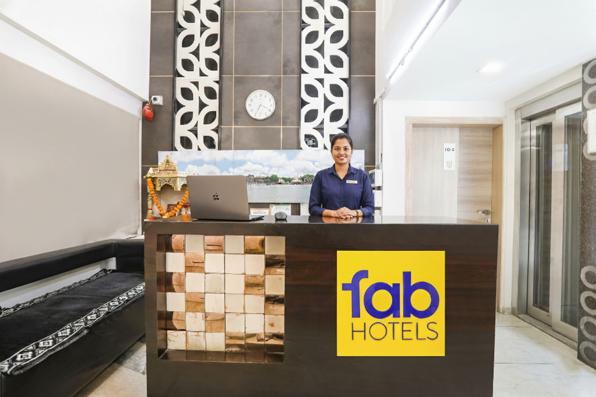 A hotel reception desk with a decorative wall, a clock, and a laptop.