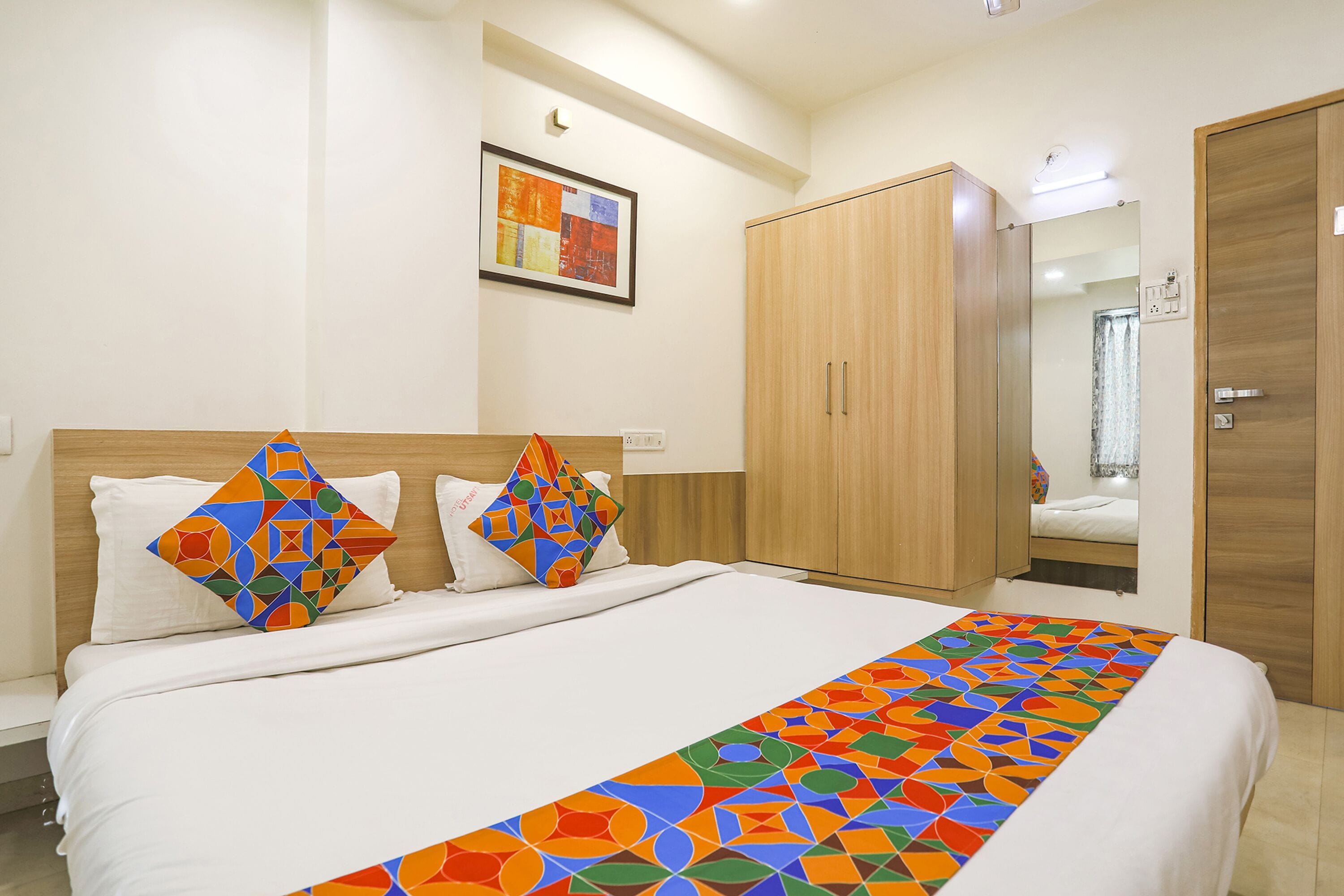 A hotel room with a large bed, wooden wardrobe, and a mirror.