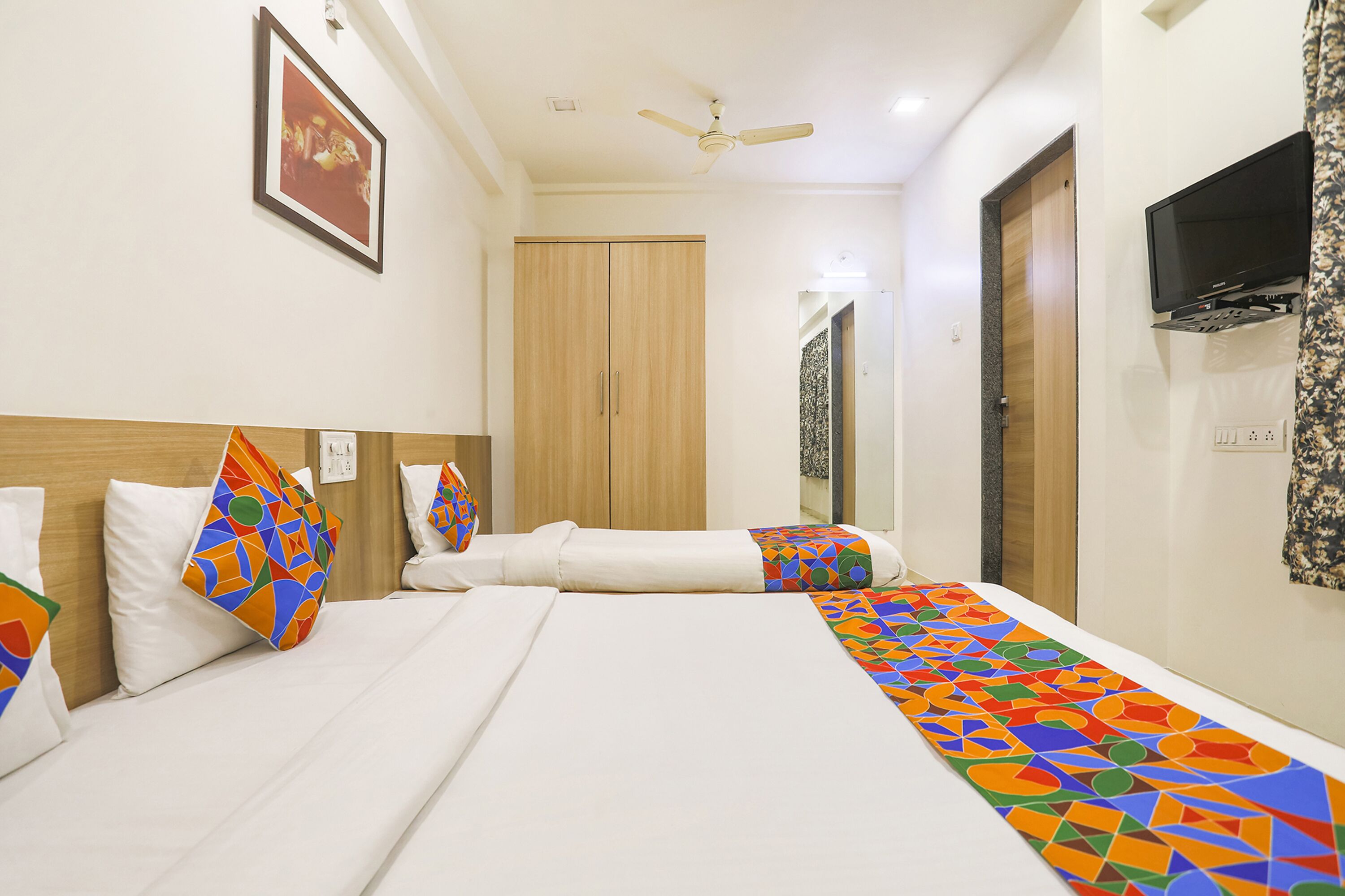 A hotel room with two beds, a ceiling fan, a TV, and a framed picture on the wall.