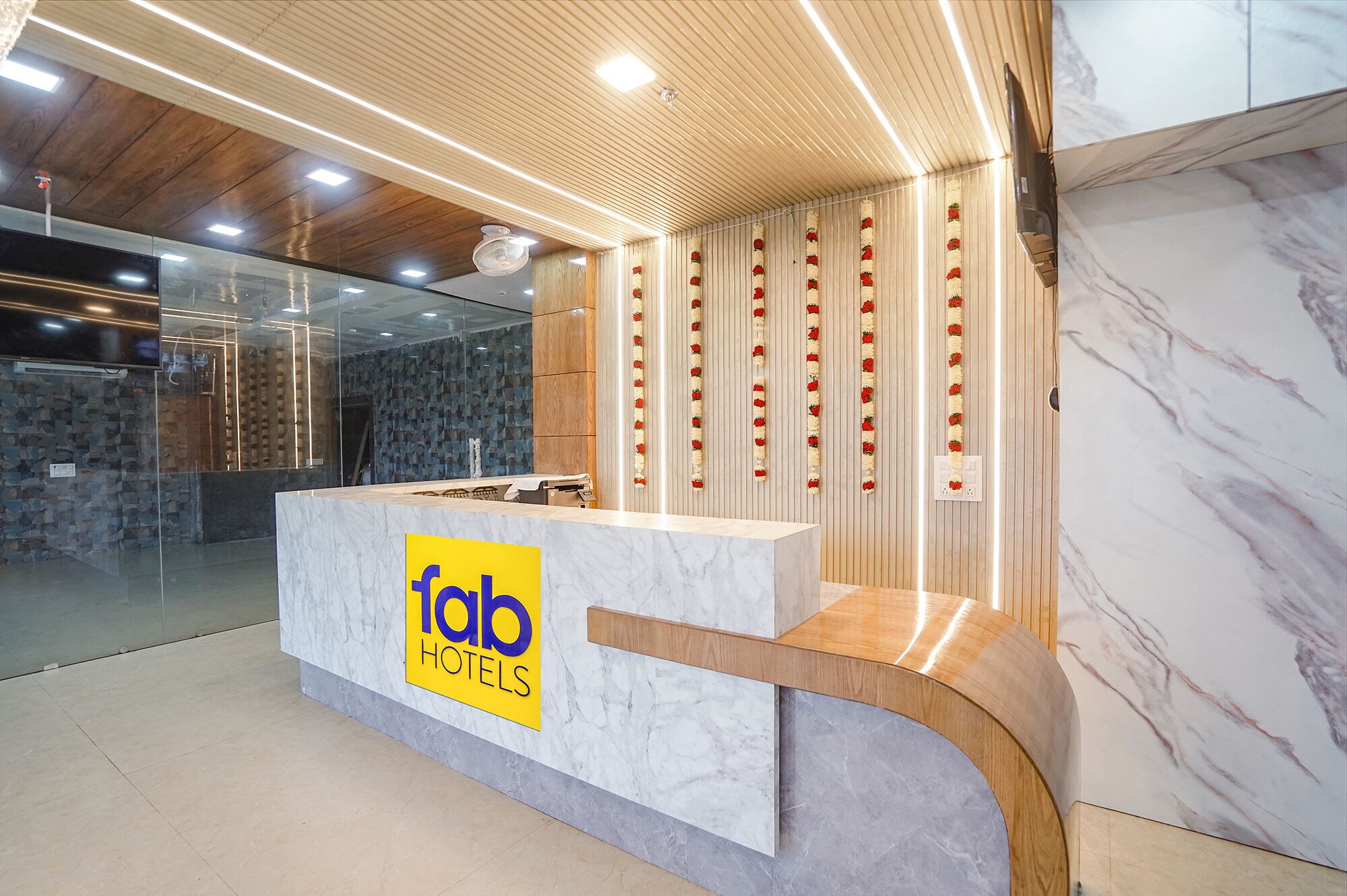 A reception desk with a marble top and a wooden base, flanked by glass walls and a wooden ceiling with recessed lighting.