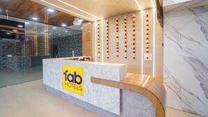 Un comptoir d’accueil doté d’un plateau en marbre et d’une base en bois, encadré de murs en verre et surmonté d’un plafond en bois avec des luminaires encastrés.