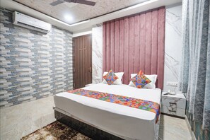 Un dormitorio con una cama, una mesita de noche, un aire acondicionado instalado en la pared, una puerta de madera y un papel tapiz estampado.