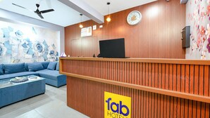 A hotel reception area with a wooden reception desk, a blue sofa, and a wall with floral artwork. - FabHotel Blue Stone Stay (Gurugram)