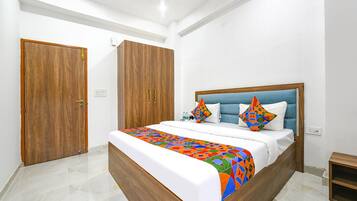 A hotel room with a bed, wooden wardrobe, and a small wooden shelf.