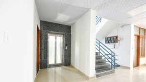 A hallway with a marble floor, a door with a frosted glass panel, and a staircase with blue railings leading to an upper level. - FabHotel Blue Stone Stay (Gurugram)