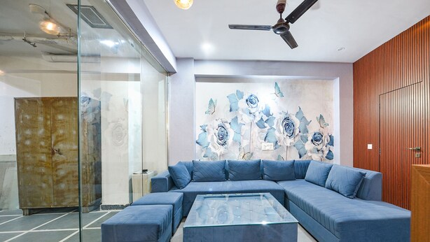 A modern living room with a sectional sofa, a glass coffee table, and a decorative wall with floral patterns. - FabHotel Blue Stone Stay (Gurugram)