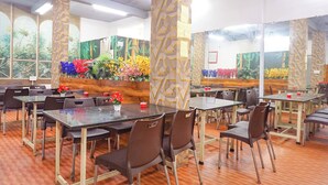 A dining area with tables and chairs, a decorative wall with geometric patterns, and a view of greenery through large windows. - FabHotel Silver Key (Pune)