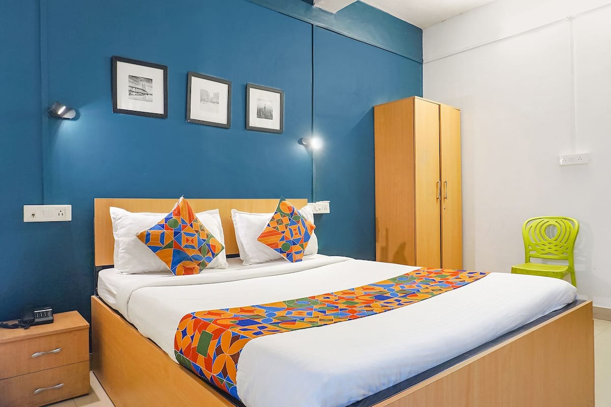 Hotellihuone, jossa on sänky, vaatekaappi, tuoli ja kolme kehystettyä kuvaa seinällä.