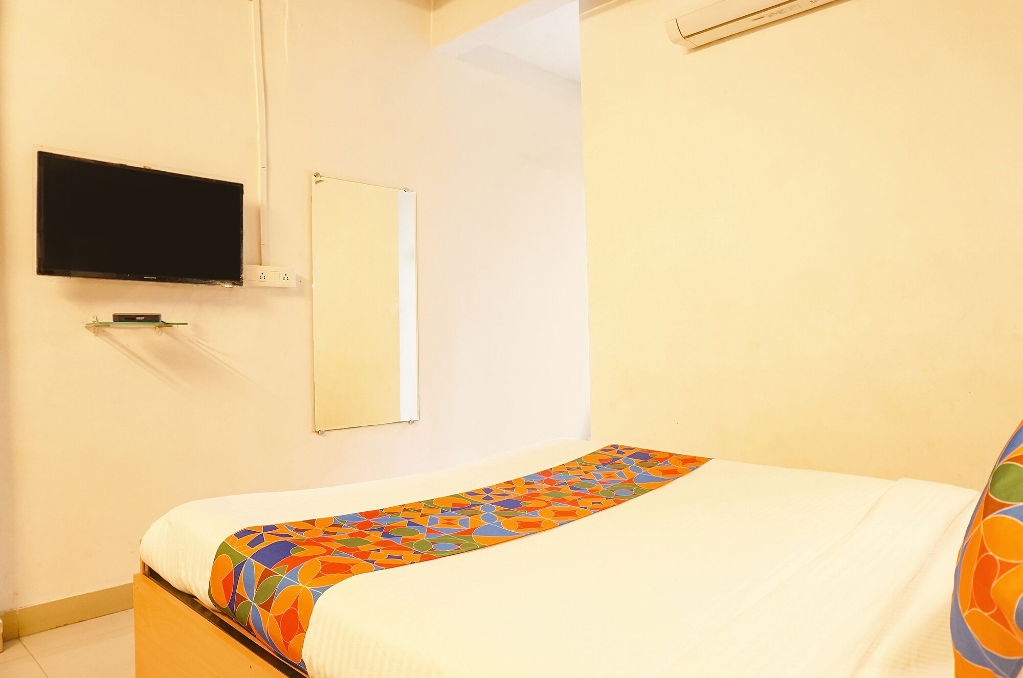 A small, simple room with a bed, a television mounted on the wall, and a mirror.