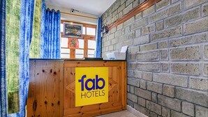A reception desk with a 'fab hotels' sign, wooden paneling, a brick wall, and a window with curtains. - Fabhotel Arigato Cottage (Manali)