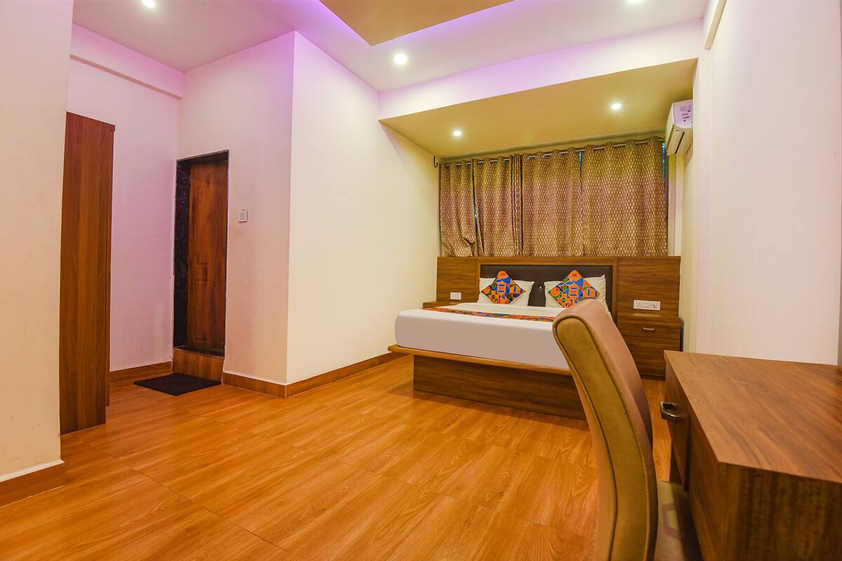 A bedroom with a wooden floor, a bed with a headboard, a bedside table, and a chair.