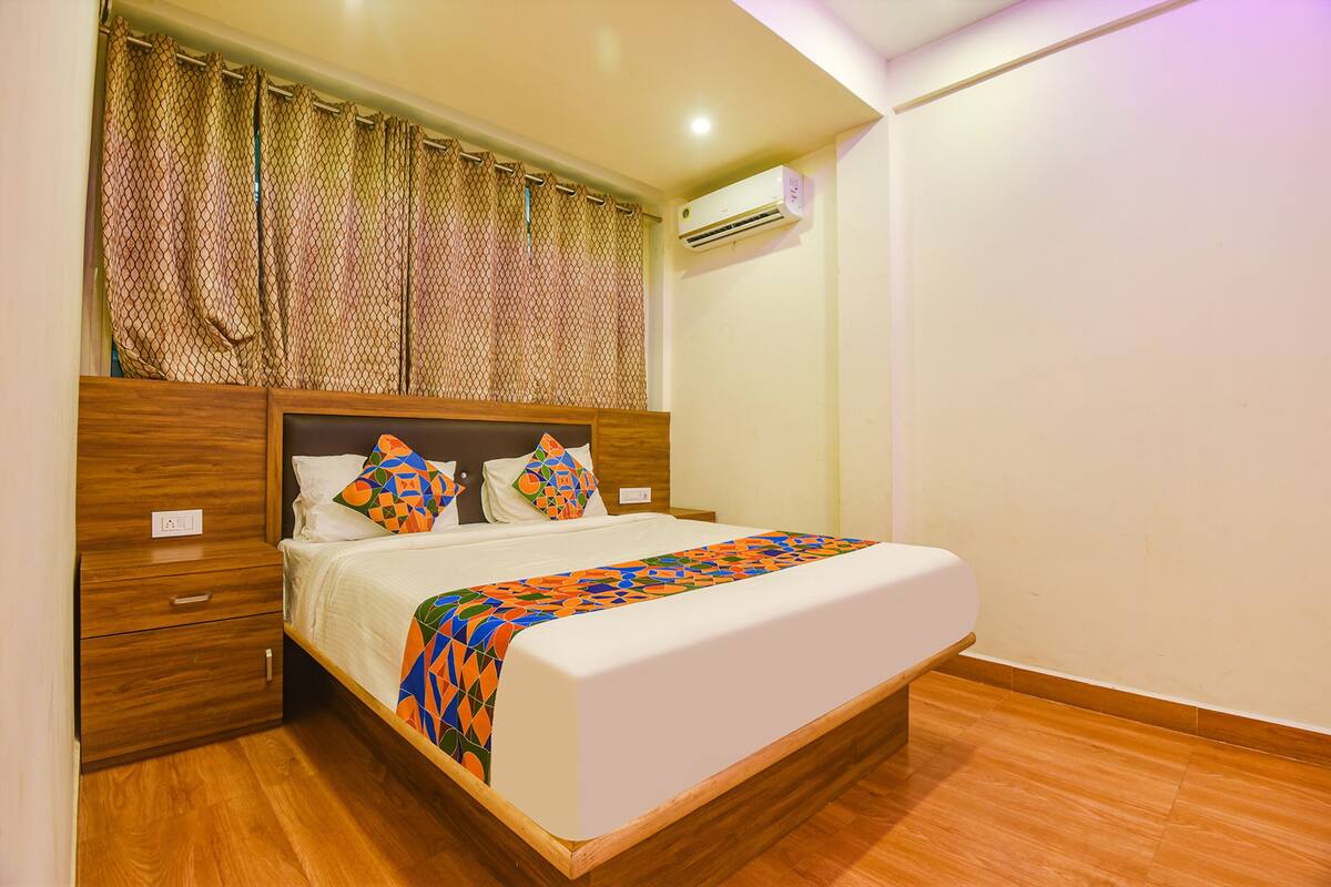 A neatly made bed with a patterned bedspread, a wooden headboard, and a nightstand with a drawer.