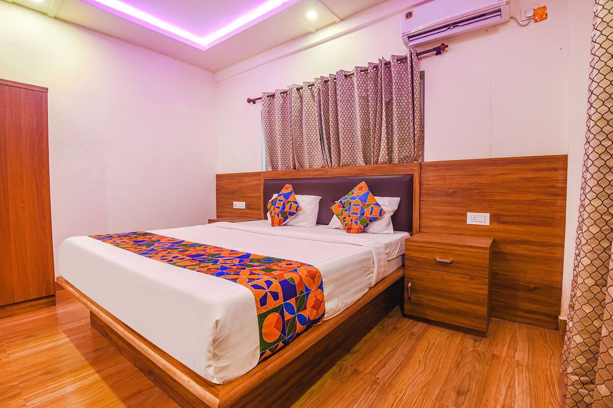 A neatly made bed with a colorful geometric-patterned blanket, a wooden headboard, and a bedside table with a drawer.