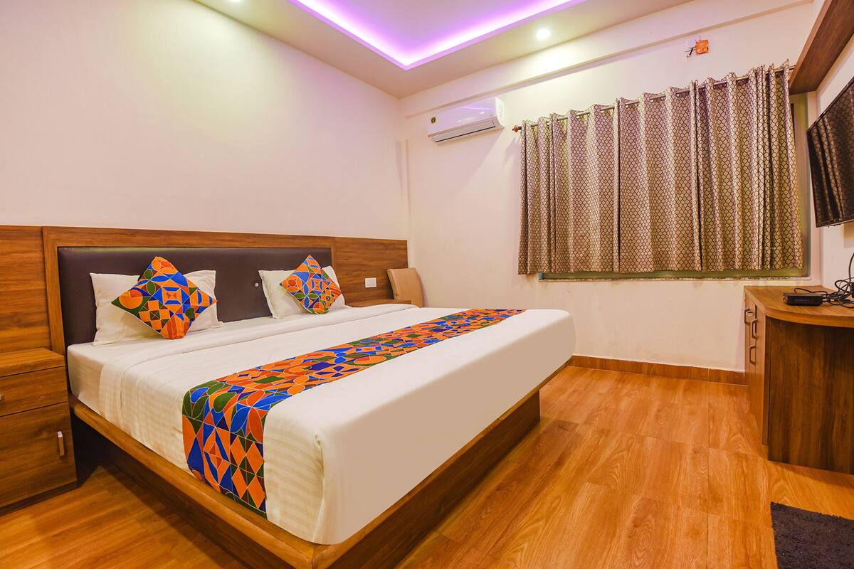 A neatly made bed with a colorful geometric throw, a wooden headboard, and a bedside table with a power strip.