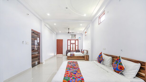 A hotel room with a large bed, a wooden headboard, and a colorful bed runner. There is a wooden door and a window with a view of the outside. - Fabhotel Shristi Homestay (Faizabad)
