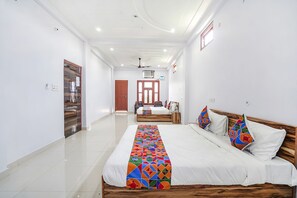 A hotel room with a large bed, a wooden headboard, and a colorful bed runner. There is a wooden door and a window with a view of the outside. - Fabhotel Shristi Homestay (Faizabad)