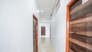 A hallway with white walls, wooden doors, and a tiled floor. - Fabhotel Shristi Homestay (Faizabad)