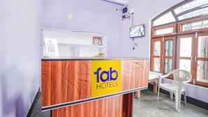 A reception desk with a 'Tab Hotels' sign, a white chair, and a window with barred glass. - Fabhotel Shristi Homestay (Faizabad)
