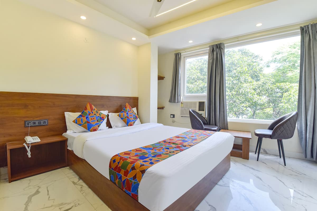 A hotel room with a large bed, a desk, a chair, a phone on the nightstand, and a window with curtains.