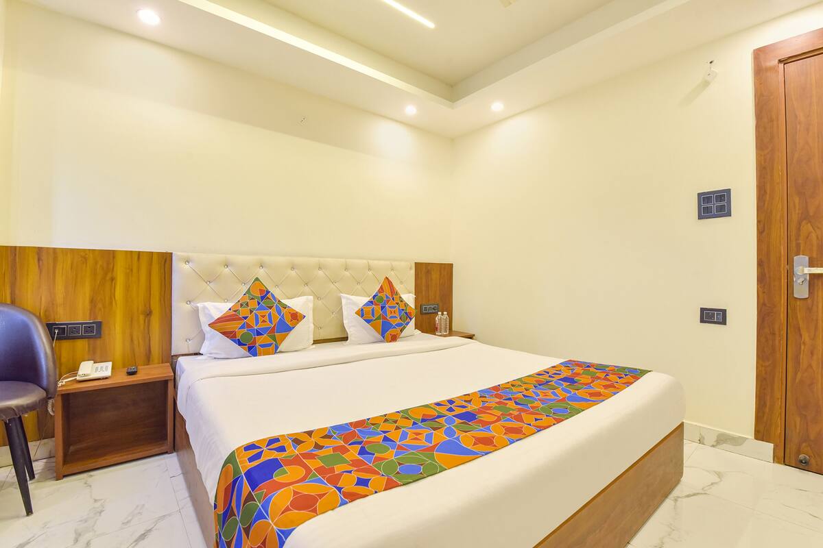 A hotel room with a bed, a wooden headboard, a nightstand with a phone, and a chair.