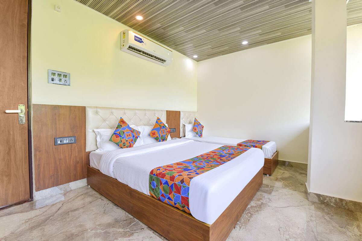 A hotel room with two beds, a wooden headboard, a patterned bedspread, and an air conditioning unit on the ceiling.