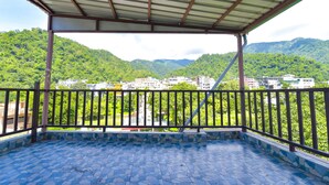 A covered balcony with a view of a green hillside and buildings. - Fabhotel Uv (Rishikesh)