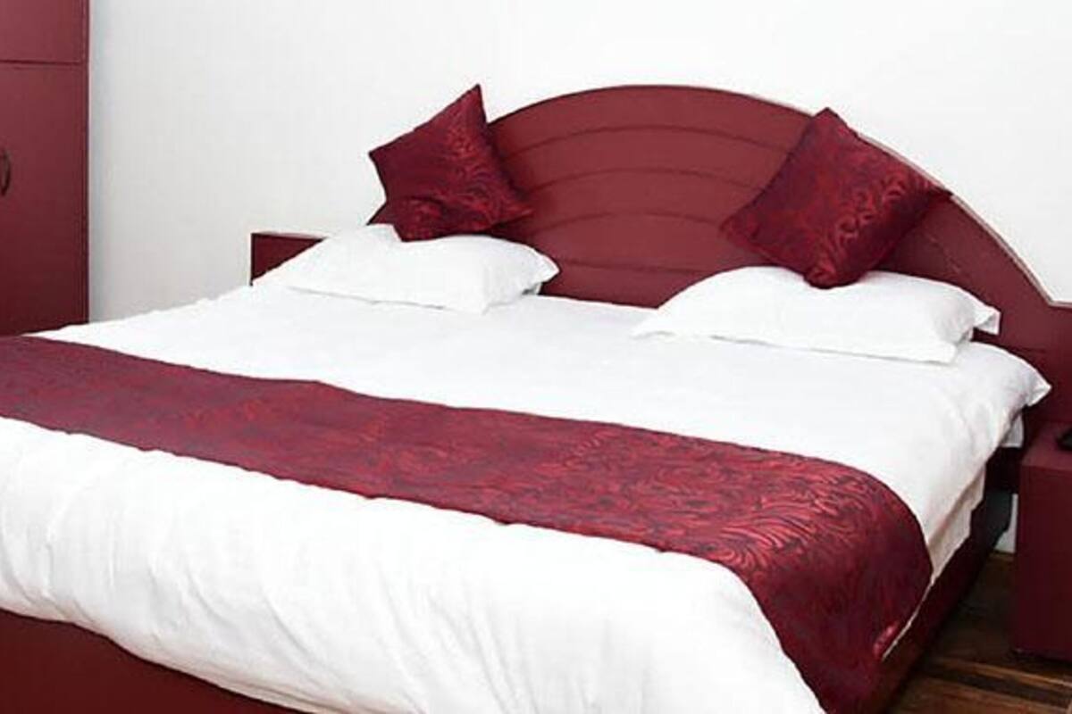Un letto rifatto con lenzuola bianche e rosse, una testata in legno e un comodino abbinato con un oggetto blu sopra.