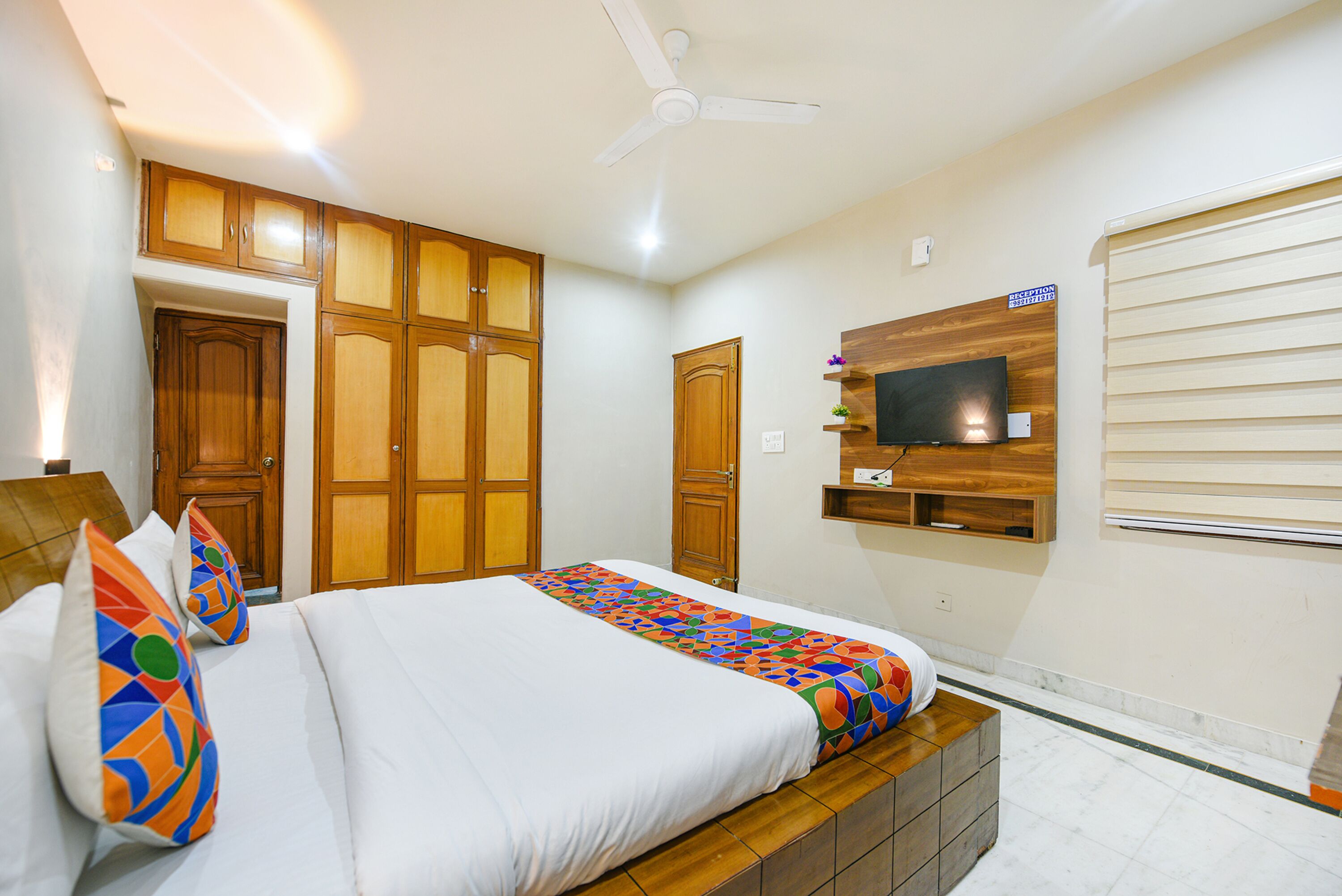 Una habitación de hotel con cama, armario de madera, televisor montado en la pared y ventilador de techo.