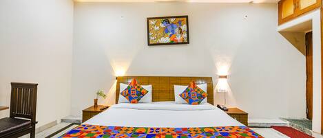 A hotel room with a large bed, two nightstands, a wooden headboard, a wall-mounted artwork, and a chair.