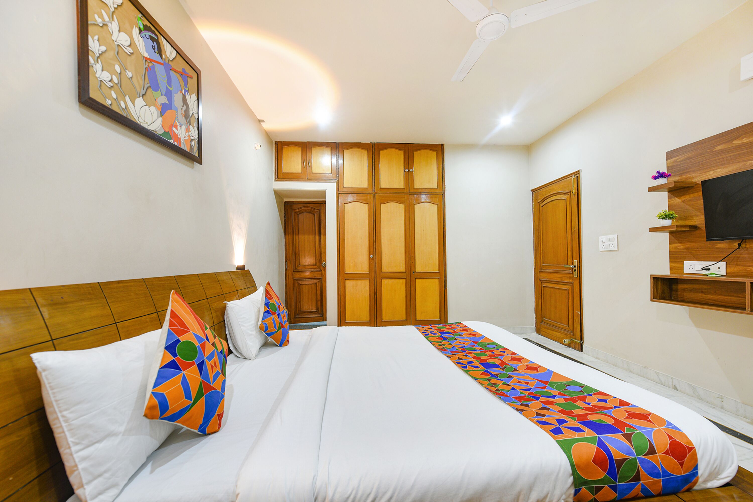A hotel room with a bed, a ceiling fan, wooden wardrobes, and a TV on the wall.