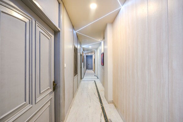 A hallway with doors on both sides, a marble floor, and recessed lighting. - FabExpress Galaxy II (Faridabad)