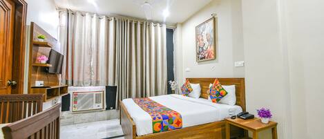 A hotel room with a wooden bed, a bedside table with a phone and a vase of flowers, a ceiling fan, and a window with curtains.
