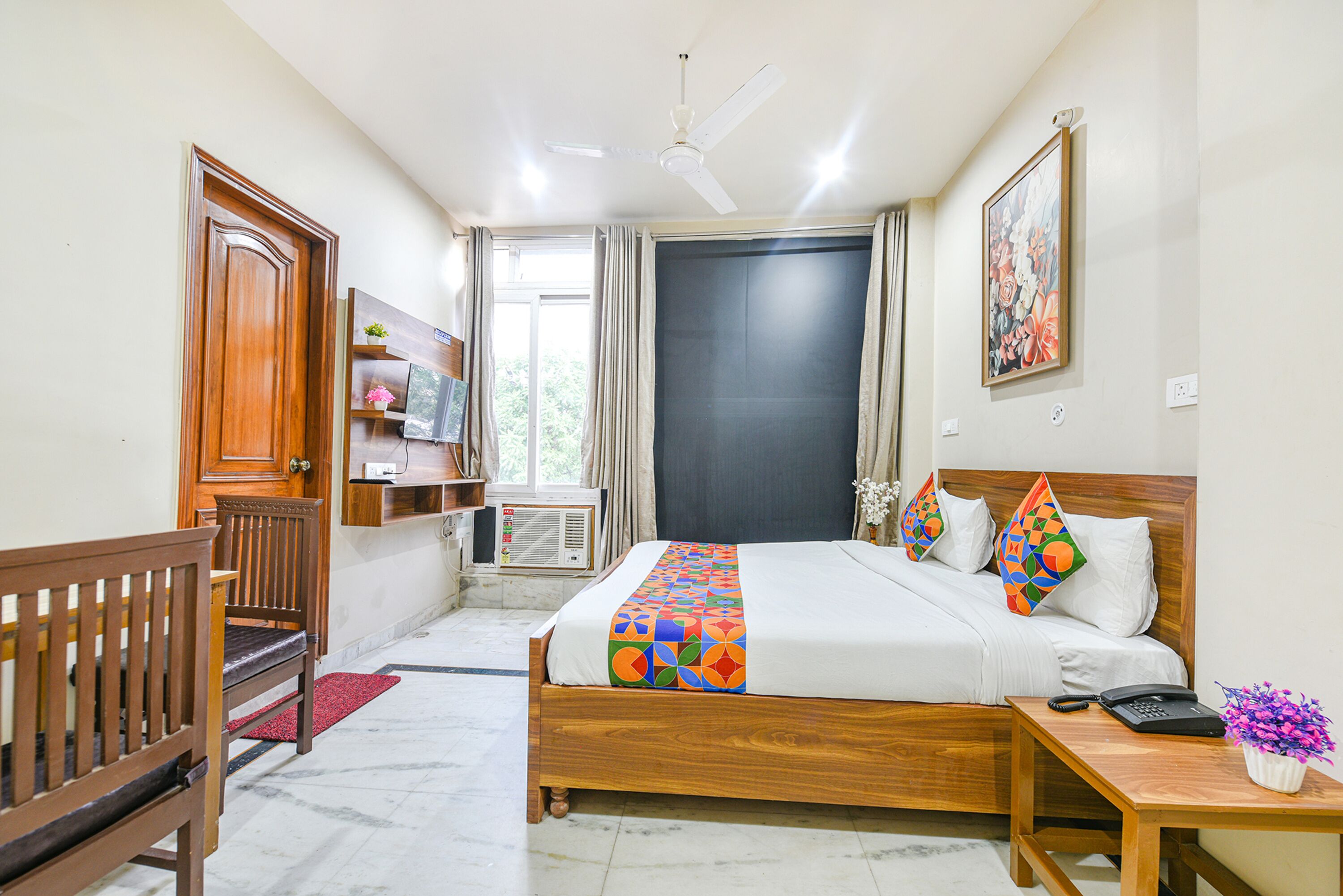 A hotel room with a wooden bed, a desk, a chair, a TV, and a window with curtains.