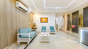 Eine moderne Lobby mit Wandverkleidung aus Holz, einer weißen Klimaanlage, einer Buddha-Statue, einem gerahmten Kunstwerk und einem Empfangstresen.