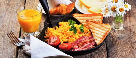 Ein Frühstücksteller mit Rührei, Speck, Tomaten und Toast, dazu ein Glas Orangensaft und eine Tasse Kaffee.