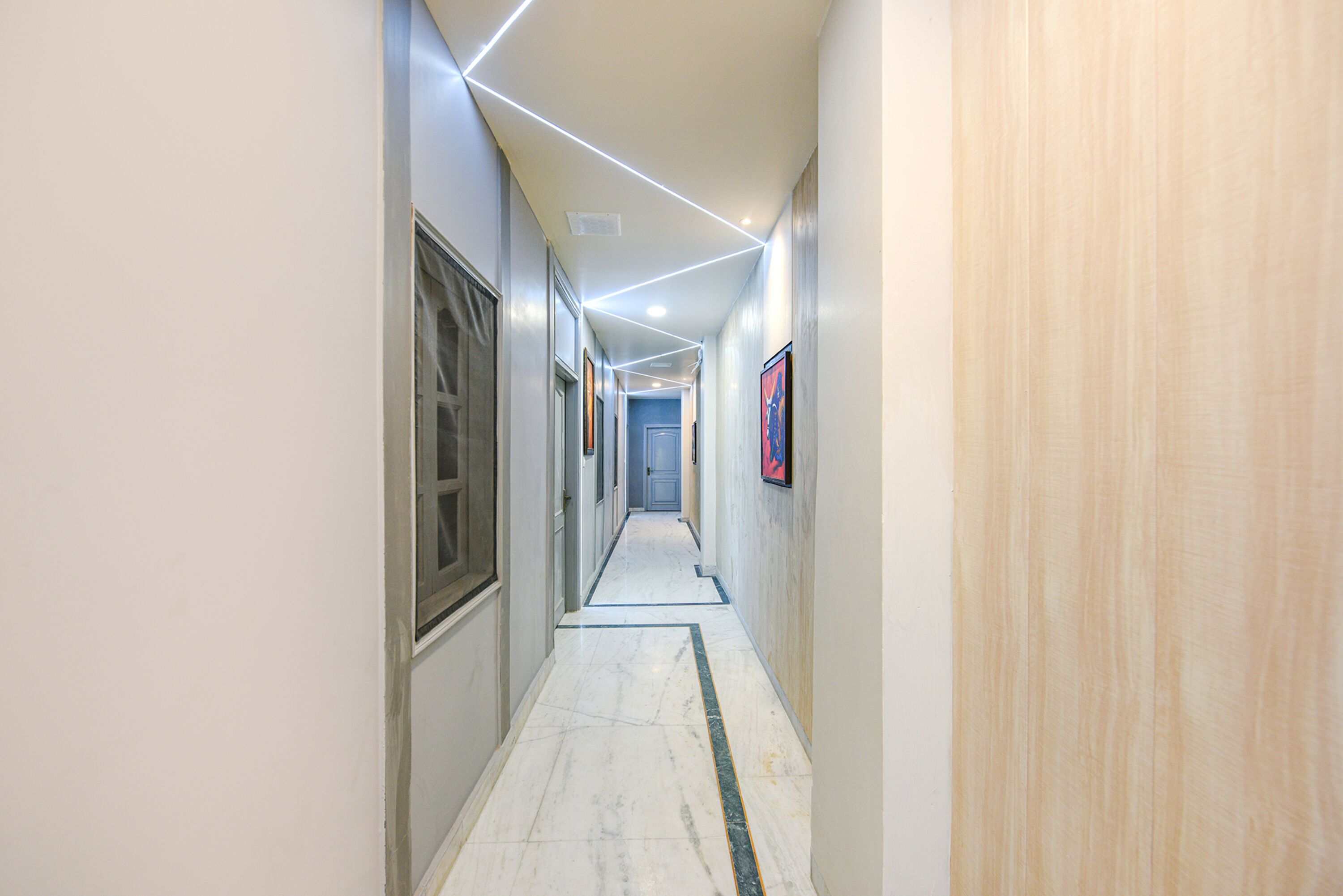 A hallway with a marble floor, light-colored walls, and a wooden panel on the right.