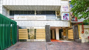 Fachada de hotel de mármol, un letrero que dice 'The Grand Palace Rooms & Banquet' y una entrada con rejas.