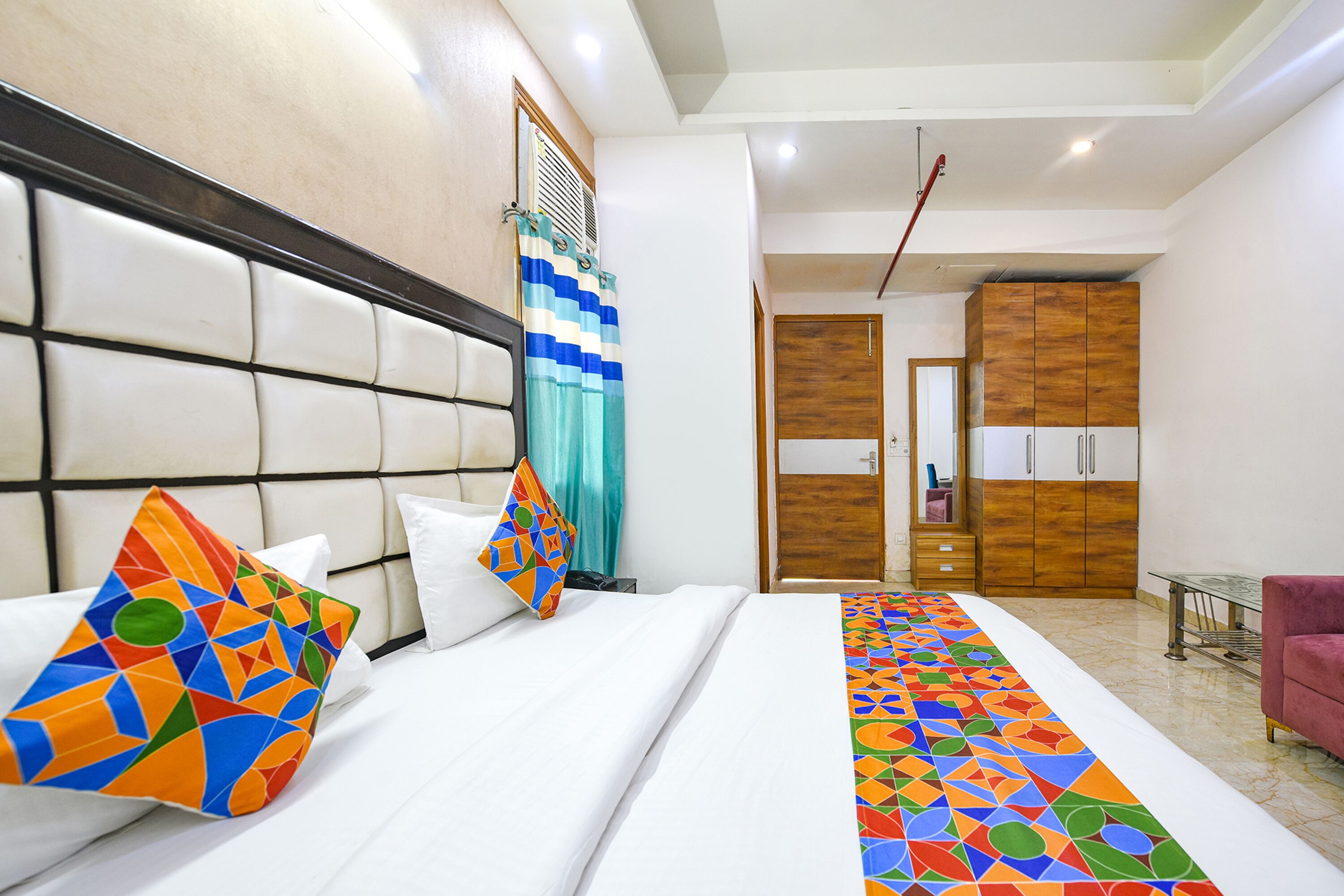 A hotel room with a large bed, a headboard, a wooden wardrobe, and a pink chair.