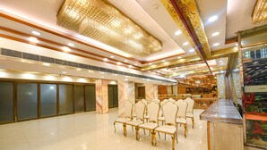 Un salón amplio con filas de sillas blancas, piso de mármol y un candelabro decorativo.