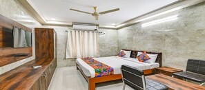 Habitación de hotel con cama, escritorio, silla, armario, ventilador de techo y aire acondicionado.