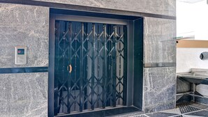 Ein moderner Aufzug mit einer geometrisch gestalteten Metalldür, einer digitalen Anzeige und einer Marmorwand.