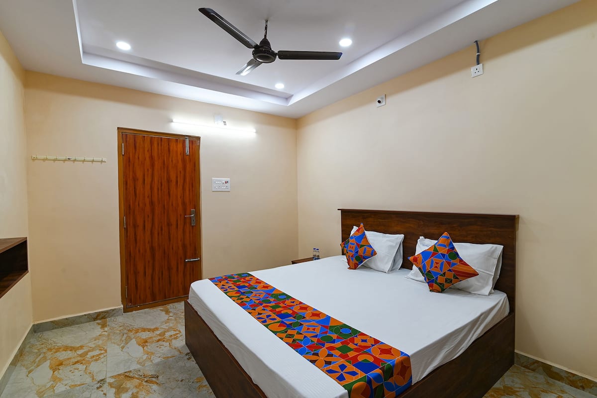 Un dormitorio con puerta de madera, cama con manta colorida, ventilador de techo e iluminación empotrada.