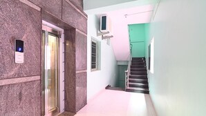 Un pasillo con pared de mármol, un ascensor, una escalera y una puerta verde.
